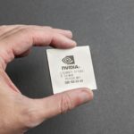 A close-up view of a person holding an Nvidia chip with a gray background.