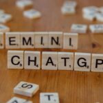 Close-up of wooden Scrabble tiles spelling Gemini and ChatGPT on a wooden surface.
