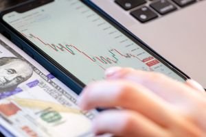 Close-up of a smartphone displaying stock market data over a dollar bill on a desk.