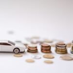White toy sports car beside stacks of coins on a white background, emphasizing savings and finance.
